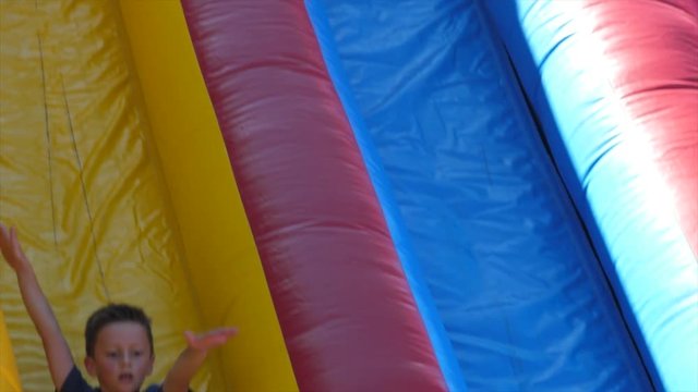 Slow motion of a boy slides down a big inflatable slide during a party