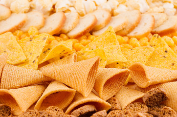 Bright spicy yellow snacks collection - popcorn, nachos, potatoes chips, croutons, corn sticks as background.