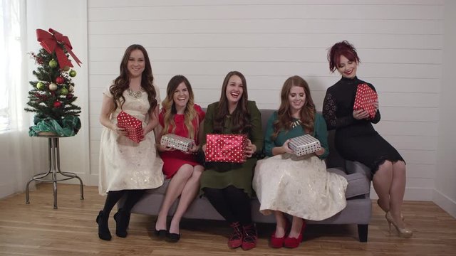 Women on couch tossing wrapped gifts into the air at the same time and laughing.