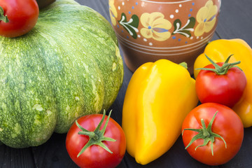Green pumpkin, tomatoes, pepper and jug on a black wooden background