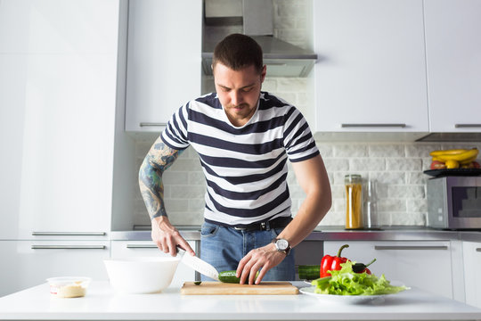 Young man preparing delicious and healthy food with vegetables in the home white kitchen