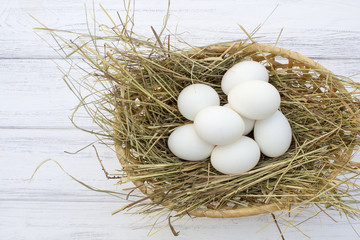 chicken eggs in basket with hay on a white wooden background. eggs on the hay