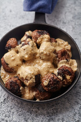 Vertical close up of traditional swedish beef meatballs with gravy served in one portion black cast iron pan, handle wrapped in blue towel. Textured background.