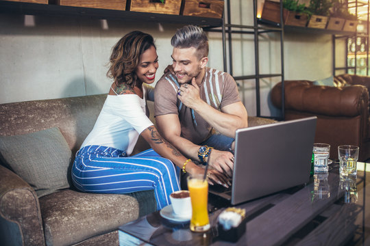 Young interracial couple spending time in cafe watching media together on laptop.