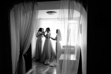 A bride getting dressed for the wedding and being helped by her bidesmaid in a dark room.