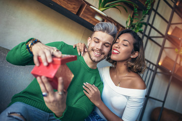 Happy  interracial couple sitting in cafe bar. Man giving gift to his girlfriend.