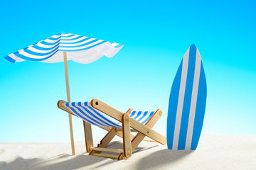 Deck chair under an umbrella and a surfboard on sandy beach
