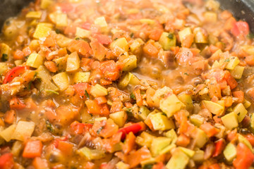 Sliced vegetables are stewed in a frying pan close up - zucchini, pepper, onions, tomatoes