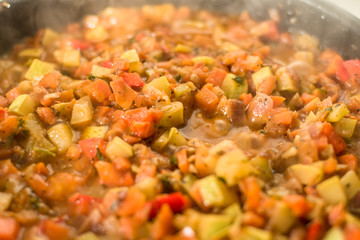 Sliced vegetables are stewed in a frying pan close up - zucchini, pepper, onions, tomatoes