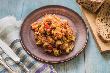 Stewed vegetables on a beautiful plate on a wooden rustic background with sliced bread - top view