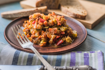 Vegetarian vegetable stew in a plate on a wooden rustic background with sliced bread - top view