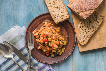 Stewed vegetables on a beautiful plate on a wooden rustic background with sliced bread - top view