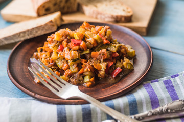 Vegetarian vegetable stew in a plate on a wooden rustic background with sliced bread - top view