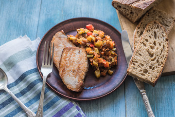 Vegetable stew and pieces of fried meat in a plate on a wooden rustic background with sliced bread - top view