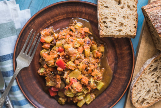 Vegetarian vegetable stew in a plate on a wooden rustic background with sliced bread - top view