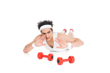 Young thin sportsman lying on floor and rejecting to exercise with dumbbells