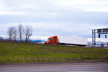 Modern big rig orange semi truck with long container trailer driving on the road