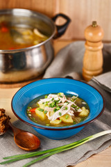 homemade chicken soup with vegetables in blue plate on wooden table.