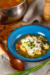homemade chicken soup with vegetables in blue plate on wooden table.