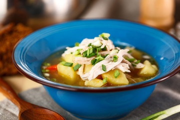 homemade chicken soup with vegetables in blue plate on wooden table.