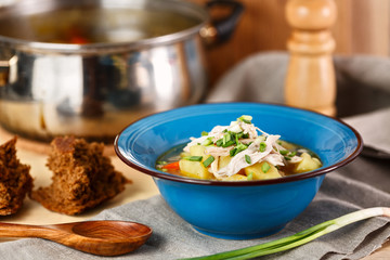 homemade chicken soup with vegetables in blue plate on wooden table.
