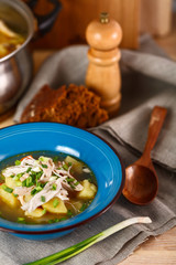homemade chicken soup with vegetables in blue plate on wooden table.