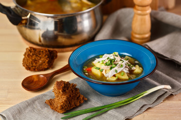 homemade chicken soup with vegetables in blue plate on wooden table.