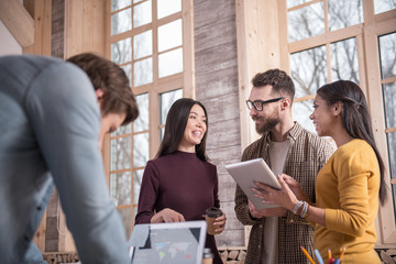 In the office. Joyful positive nice colleagues standing together and discussing their project while talking to each other