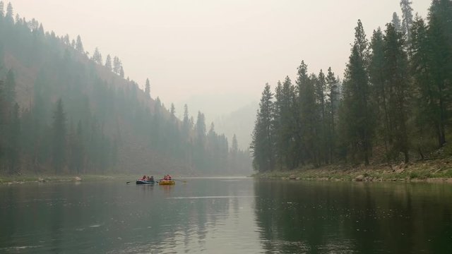 Rafts floating down a river through forrest filled with smoke