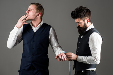 Client, businessman with arrogant face smoke cigar while tailor working.