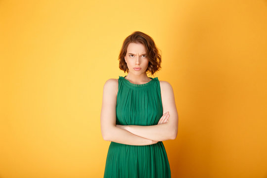 Portrait of offended woman with arms crossed looking at camera isolated on orange
