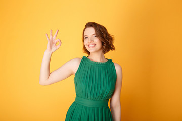 portrait of pretty smiling woman showing ok sign isolated on orange