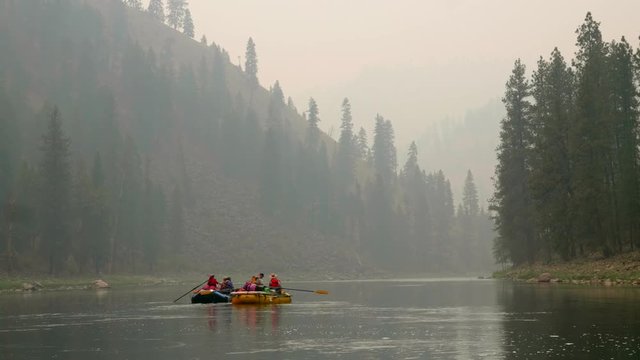 Rafts floating down river through forrest filled with smoke at sunset