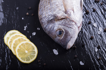 Sea bream with lemon slices, pepper corns and rock salt on a slate board.
