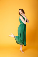 young smiling woman in green dress posing isolated on orange