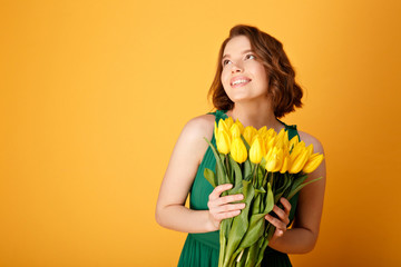 portrait pf dreamy woman with bouquet of yellow tulips isolated on orange