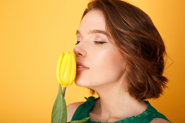 portrait of woman smelling yellow tulip isolated on orange