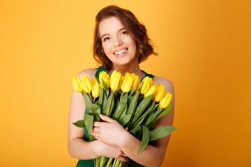 portrait of cheerful woman with bouquet of yellow spring tulips isolated on orange