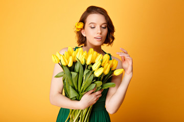 portrait of young woman looking at bouquet of yellow tulips in hand isolated on orange