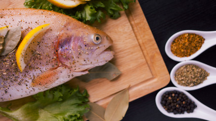 Fresh trout and ingredients to prepare fish dishes on black table