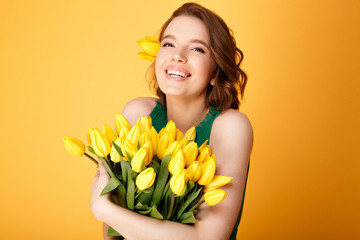 portrait of cheerful woman with bouquet of yellow tulips isolated on orange