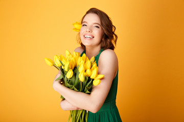 portrait of happy woman in green dress with bouquet of yellow tulips isolated on orange