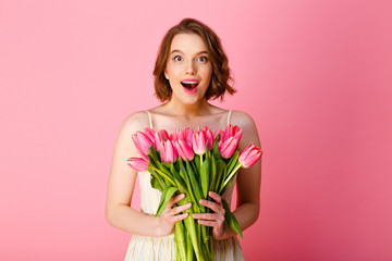 portrait of excited woman holding bouquet of pink tulips isolated on pink