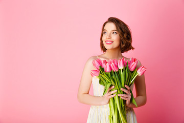 smiling woman with bouquet of pink tulips looking away isolated on pink
