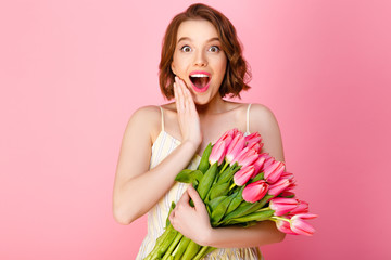 surprised woman with bouquet of spring tulips isolated on pink