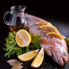 Fresh trout and ingredients to prepare fish dishes on black table