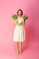 young shocked woman with bouquets of spring flowers isolated on pink