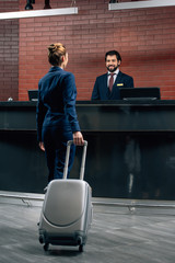 businesswoman with luggage going at hotel reception counter