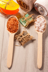 Wooden spoons with brown and white sea salt and handmade soap for bathroom procedures with towels on the background