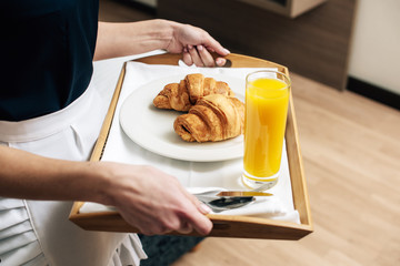 cropped shot of maid in uniform holding croissants and juice on tray